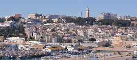 White houses of a hillside town above a harbour, with a mosque tower on the skyline