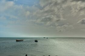 Small boats moored on a calm grey sea under a cloudy sky, seen from the shore