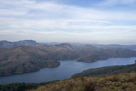 A long reservoir winding between forested hills, seen from a hilltop under a pale sky