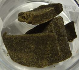 Flat greenish-brown slabs of pressed hashish in a glass jar.