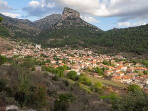 A village of pale houses below a limestone crag, at the edge of a flat cultivated plain