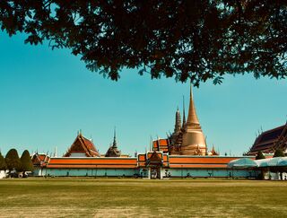 Wide-angle view of the Grand Palace in Bangkok with blue sky and lush trees, Bangkok, Thailand.