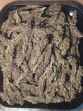 Dried purple-brown cannabis buds spread across a black tray