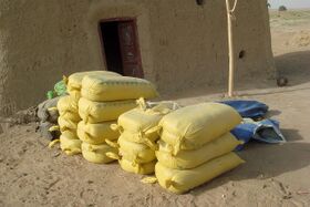 Stacks of yellow sacks tied at the neck, piled outside the door of a mud-walled building on bare sandy ground
