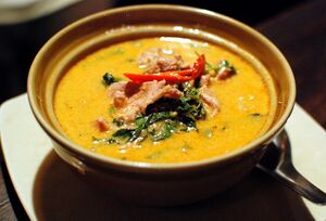 A bowl of orange-red curry with pork, red chilli and green leaves