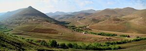 A village of small houses on a slope above terraced fields, with high bare mountains behind