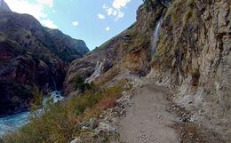 Rocky trail cut into a cliff above a fast river, with a waterfall